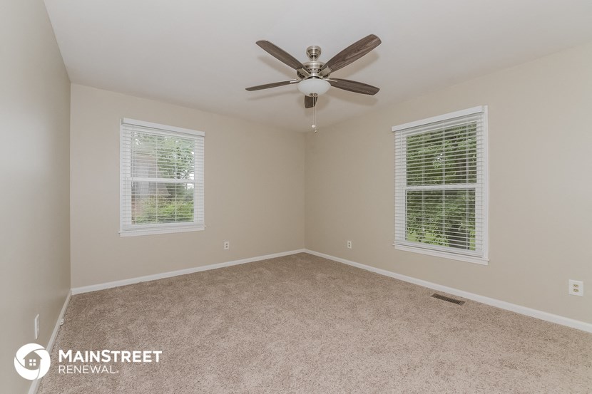 an empty room with a ceiling fan and two windows