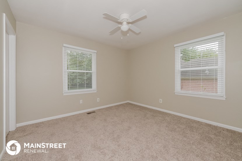 an empty bedroom with a ceiling fan and two windows