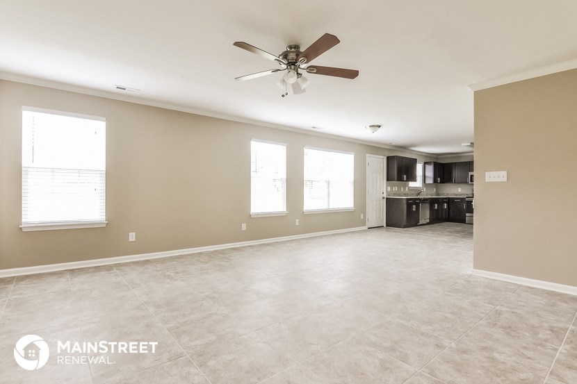 an empty living room with a ceiling fan and a kitchen