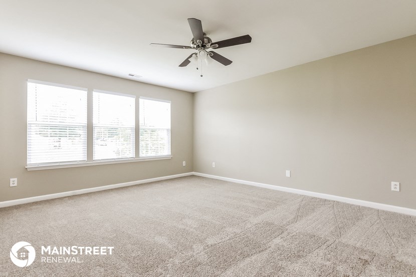 the spacious living room with ceiling fan and large windows