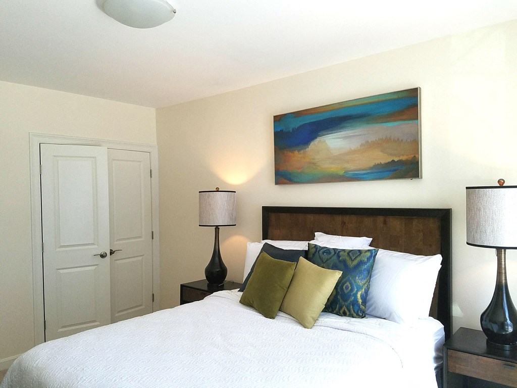 a bedroom with a bed and two lamps and a painting on the wall