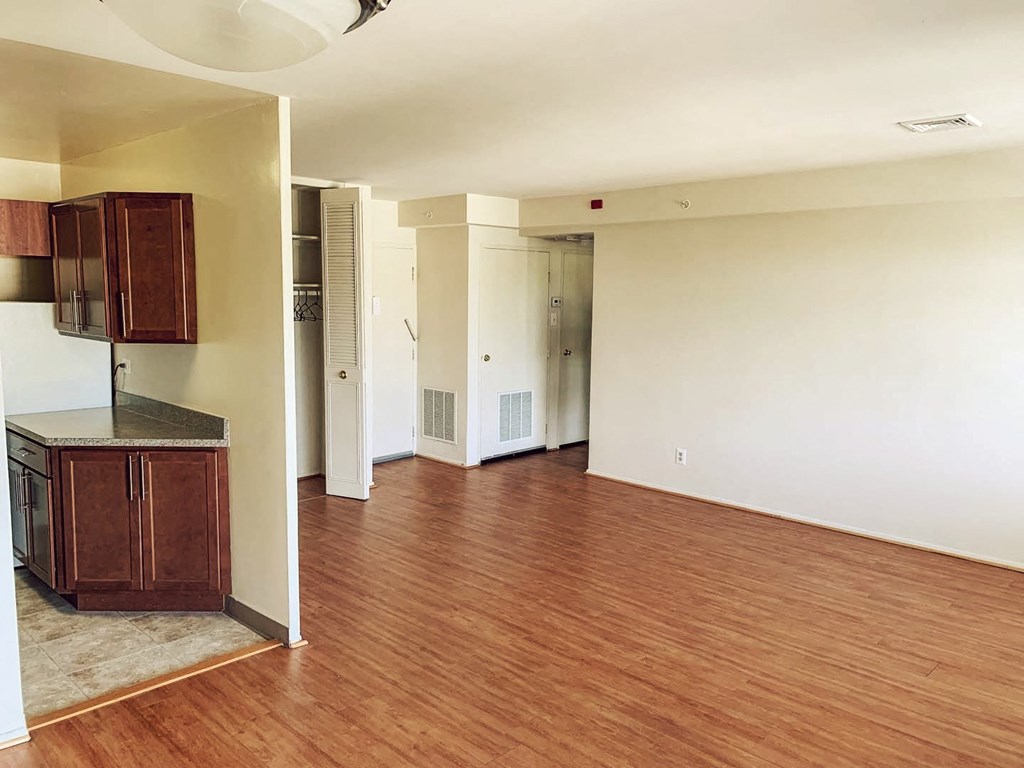 an empty living room with wood flooring and a kitchen