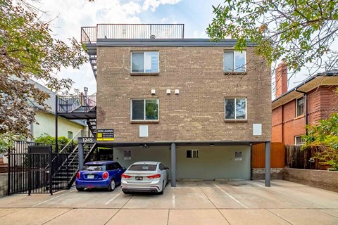 Two cars are parked in a garage in front of a brick building.