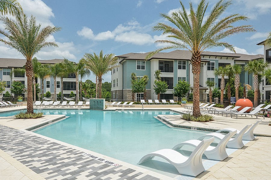 a swimming pool with chairs and palm trees in front of an apartment building