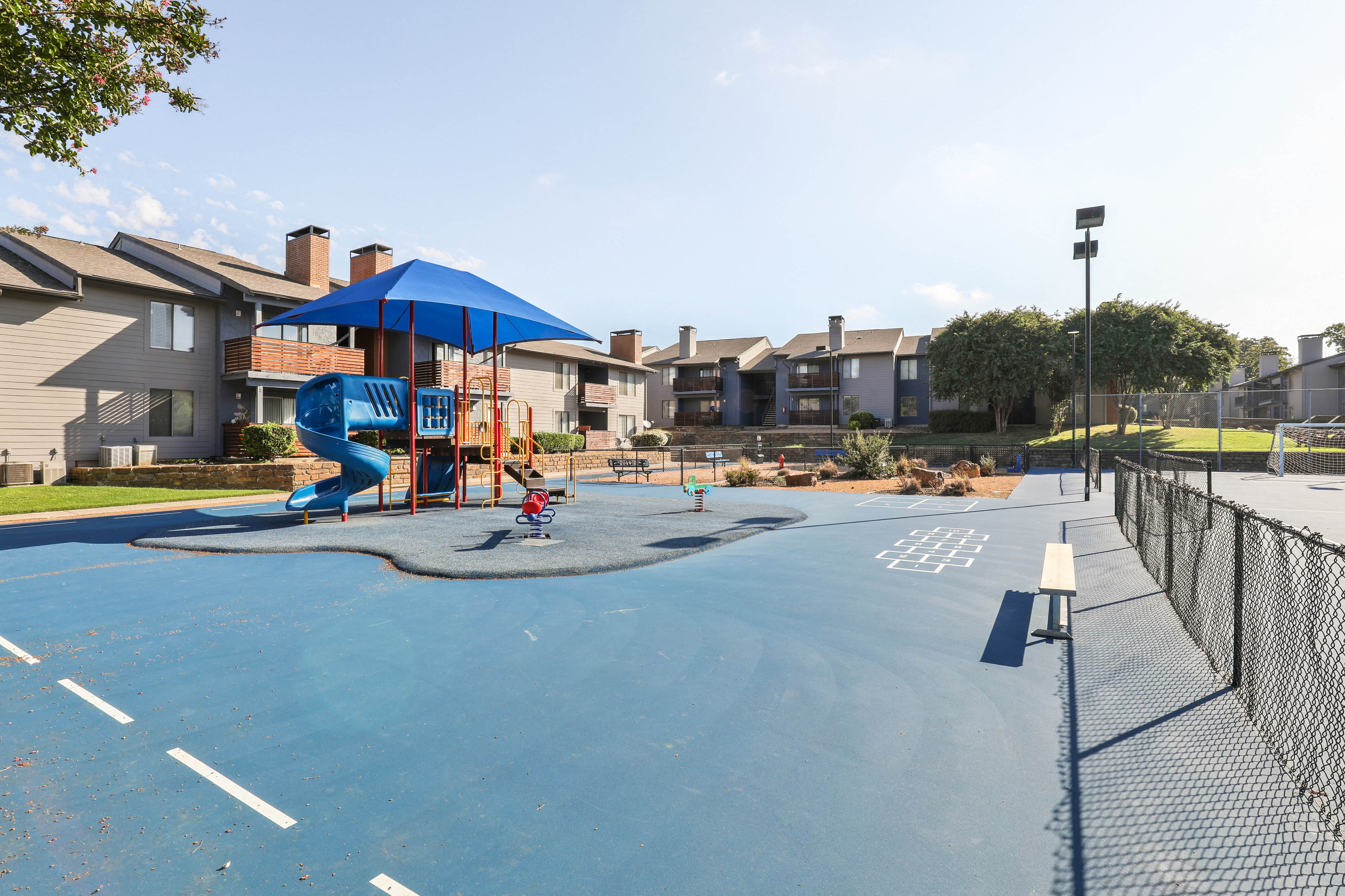 an empty basketball court with a playground and apartments in the background