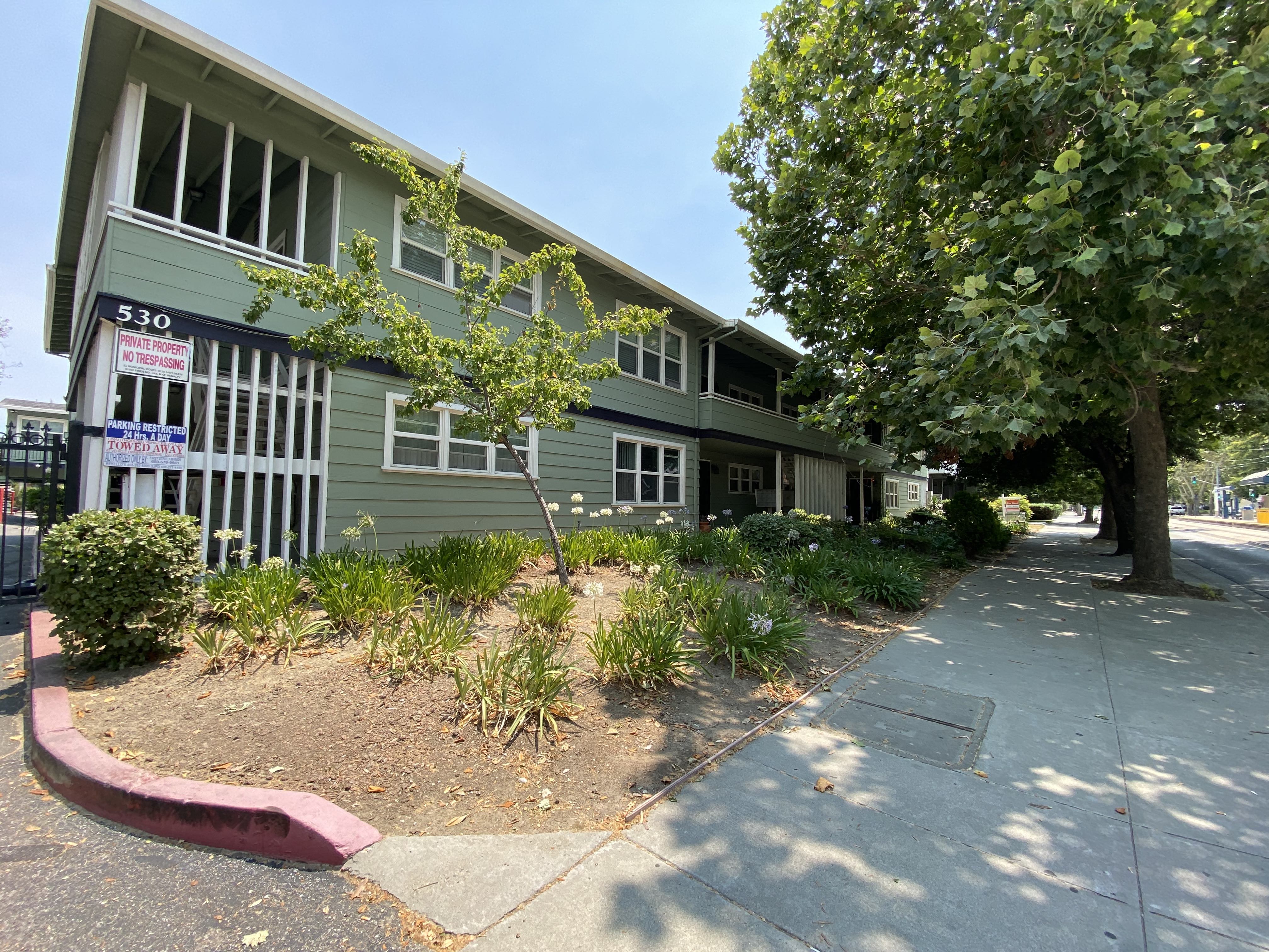 a green building with a sidewalk and trees in front of it