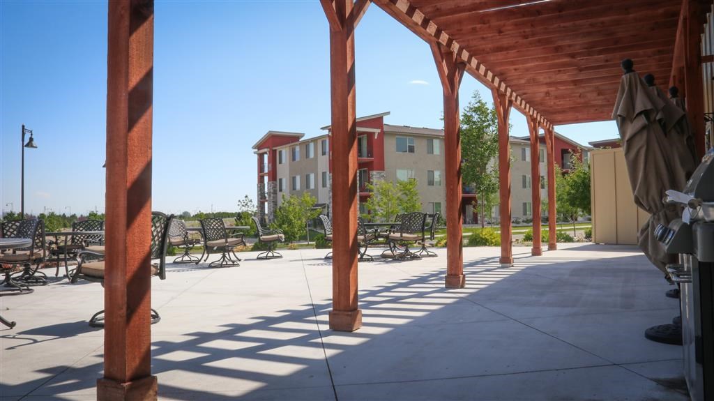 a covered patio with chairs and tables in front of an apartment building