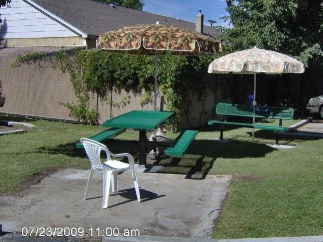 two green picnic tables with umbrellas in a backyard