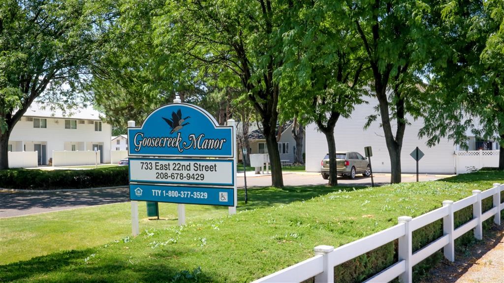 a street sign in front of a white fence and some trees