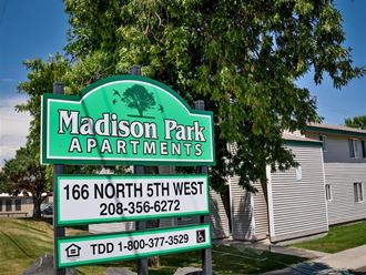 a sign for madison park apartments in front of a tree