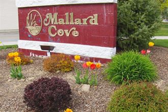 a sign for mallard cove with flowers in front of it