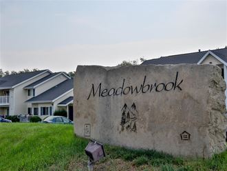 a large stone sign in the grass with houses in the background