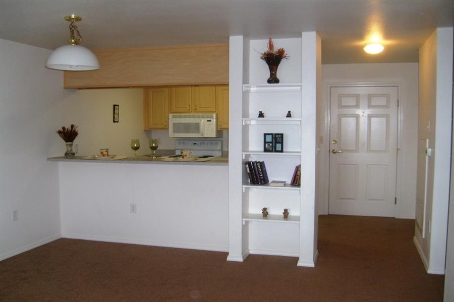 an empty living room with a kitchen and a white shelf
