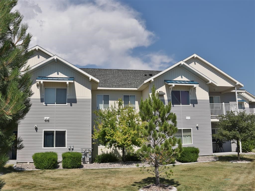 a gray house with a lawn and trees in front of it