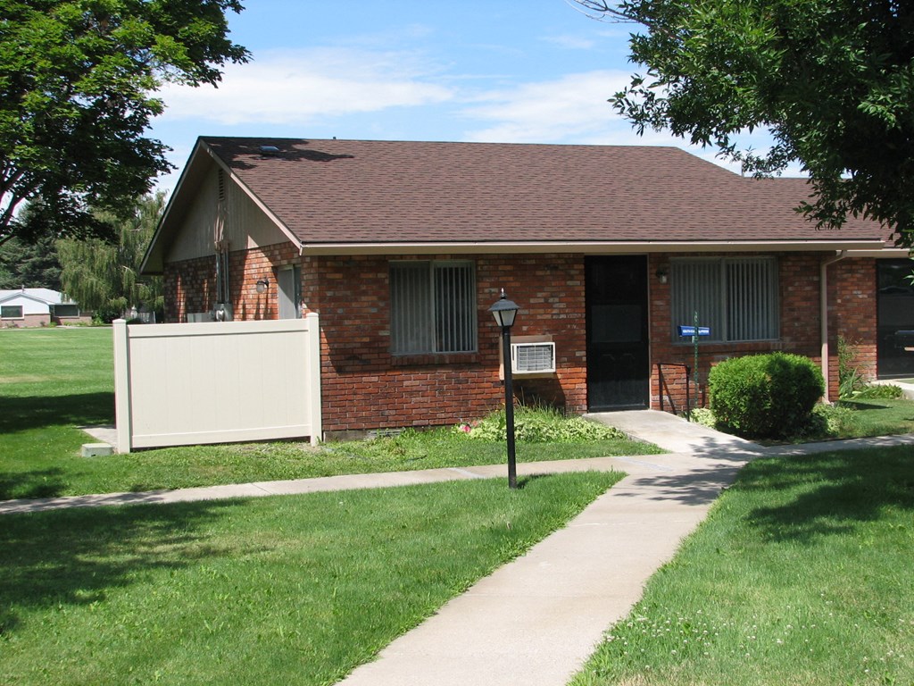 the front of a brick house with a white fence and lawn