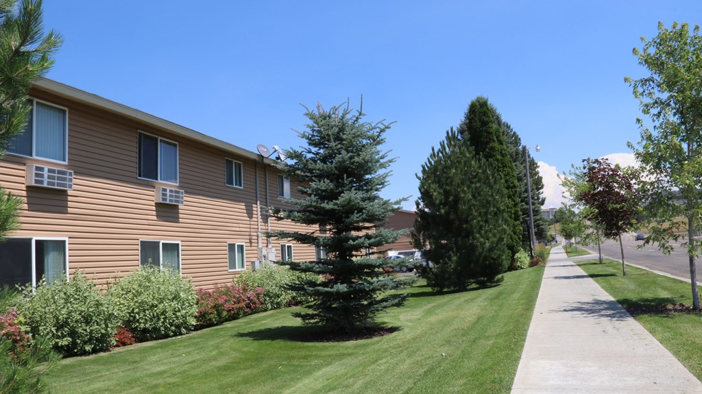 an apartment building with a sidewalk and trees in front of it