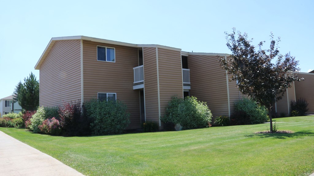 an apartment building with brown siding and a green lawn
