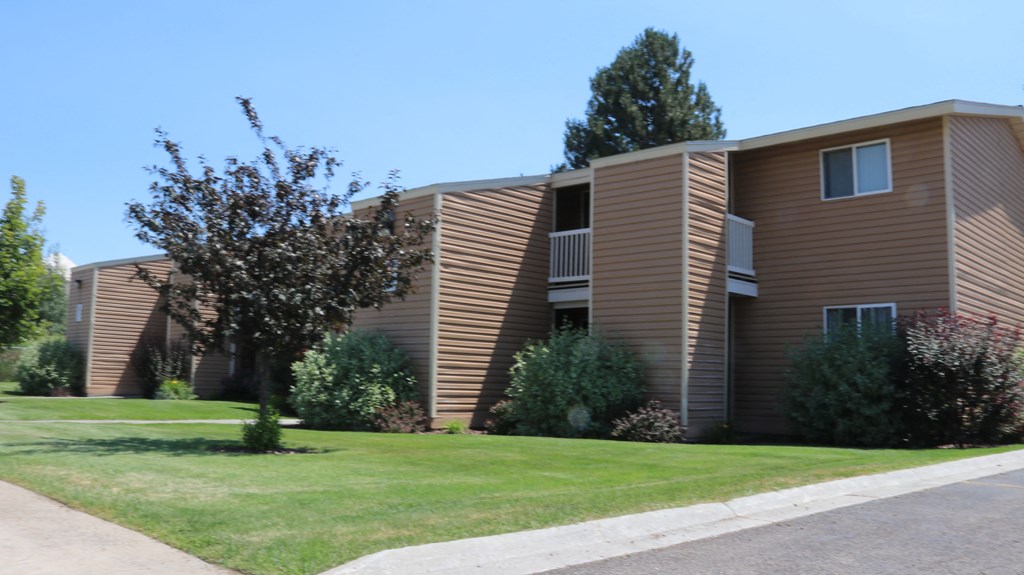 an apartment building with brown siding and green grass and trees