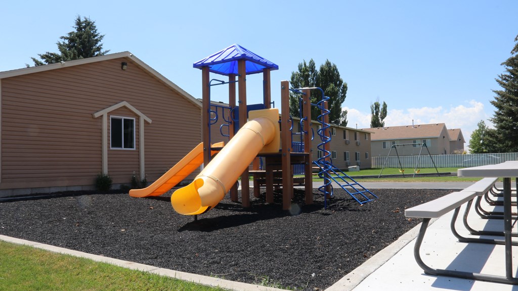 a playground with a slide and a picnic table in front of a building