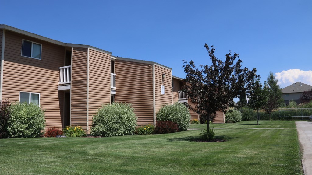 an apartment building with a green lawn and trees