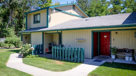 the front of a yellow house with a red door and a green fence