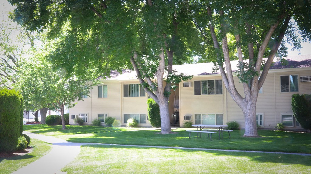 a large yellow apartment building with trees and a sidewalk