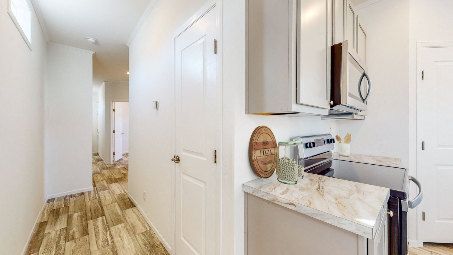 a kitchen with white cabinets and a white counter top and a hallway in the background