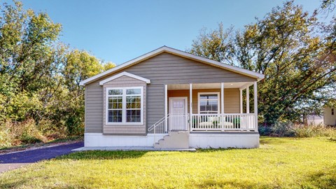 a small brown house with a porch and a lawn
