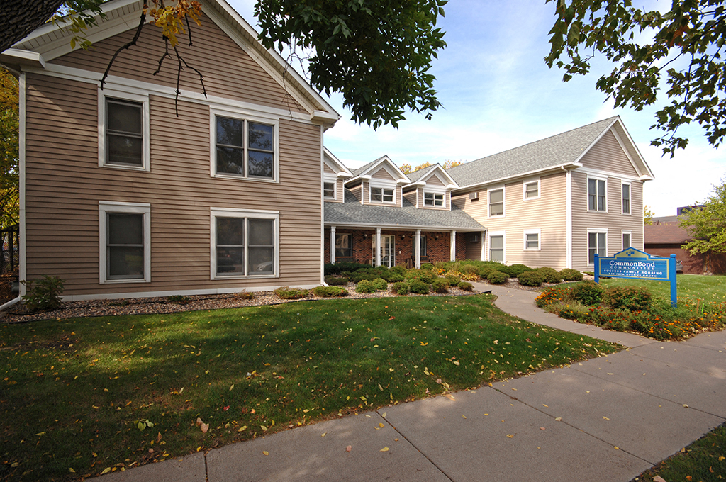 a sidewalk in front of a house with a yard and a blue sign