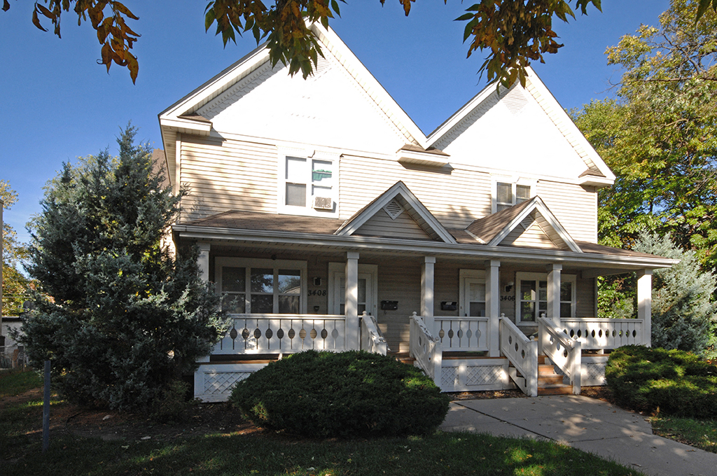 the front of a white house with a porch and a tree