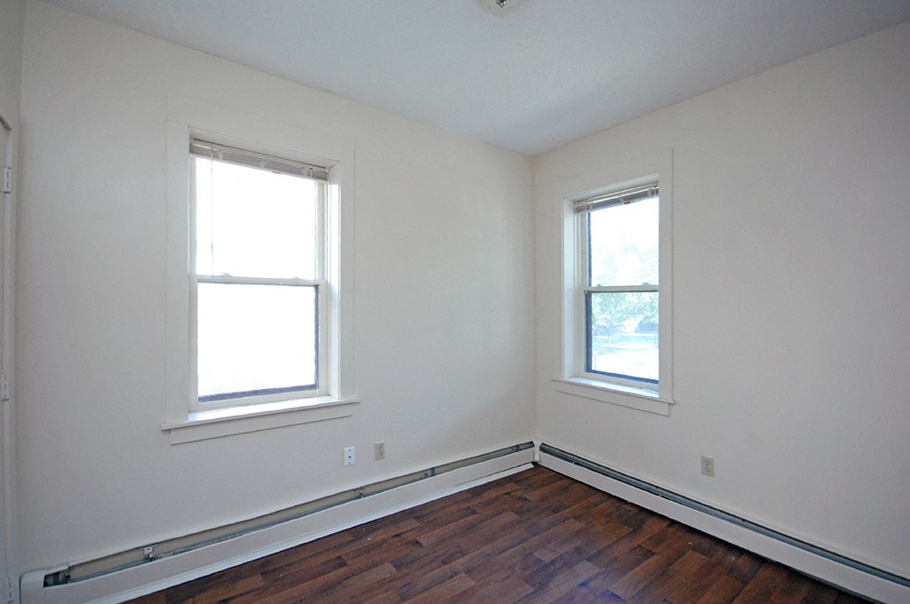 a bedroom with white walls and two windows and a wooden floor