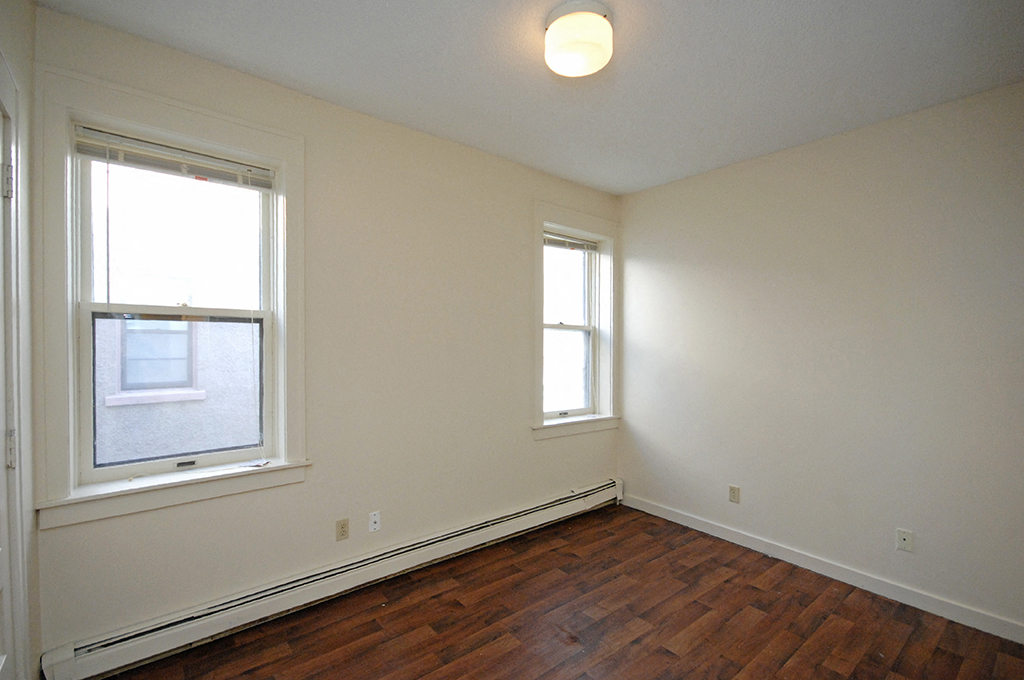 an empty room with wood flooring and two windows