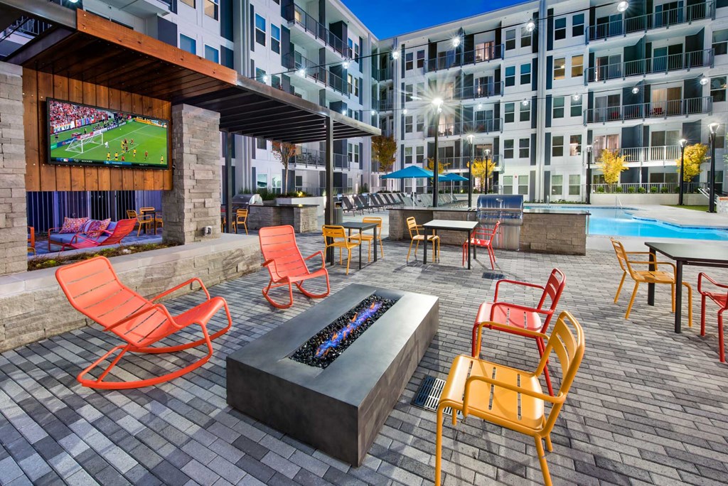 an outdoor lounge area with a fire pit and a tv in an apartment building