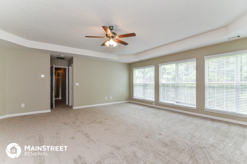 an empty living room with large windows and a ceiling fan