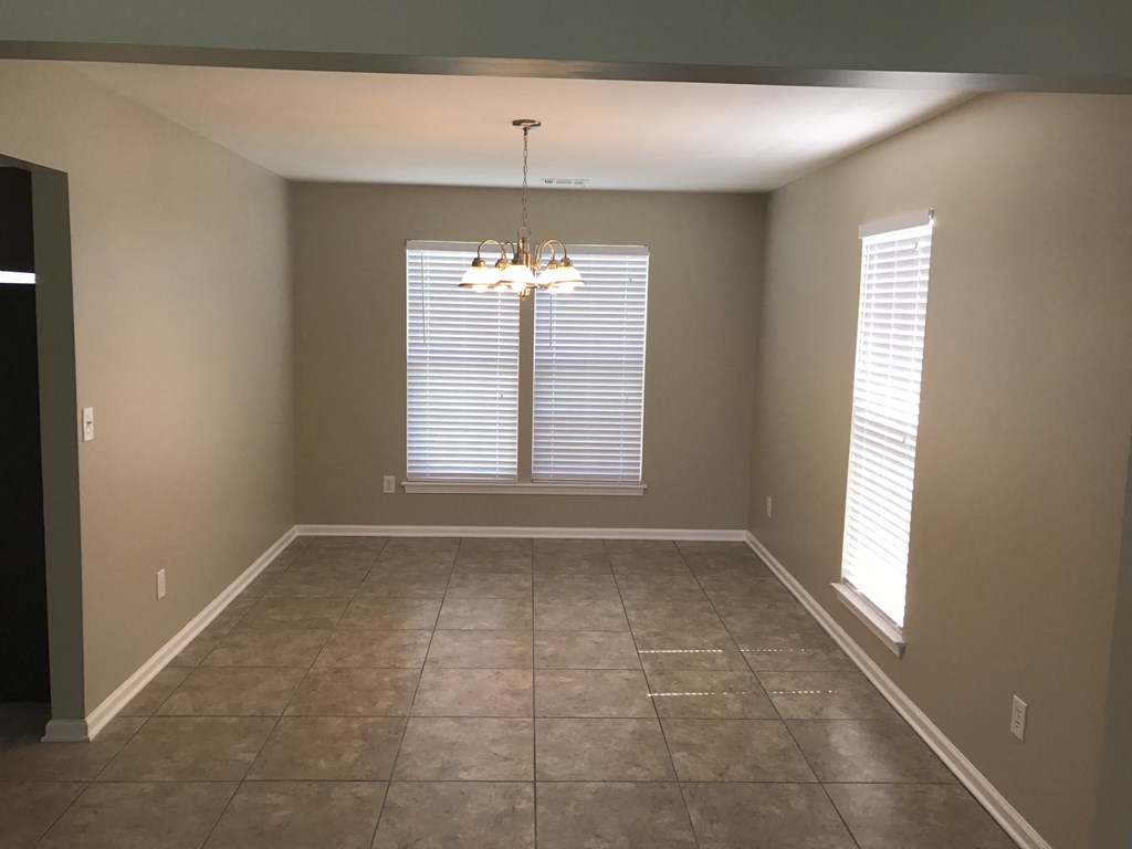 an empty dining room with a window and a chandelier