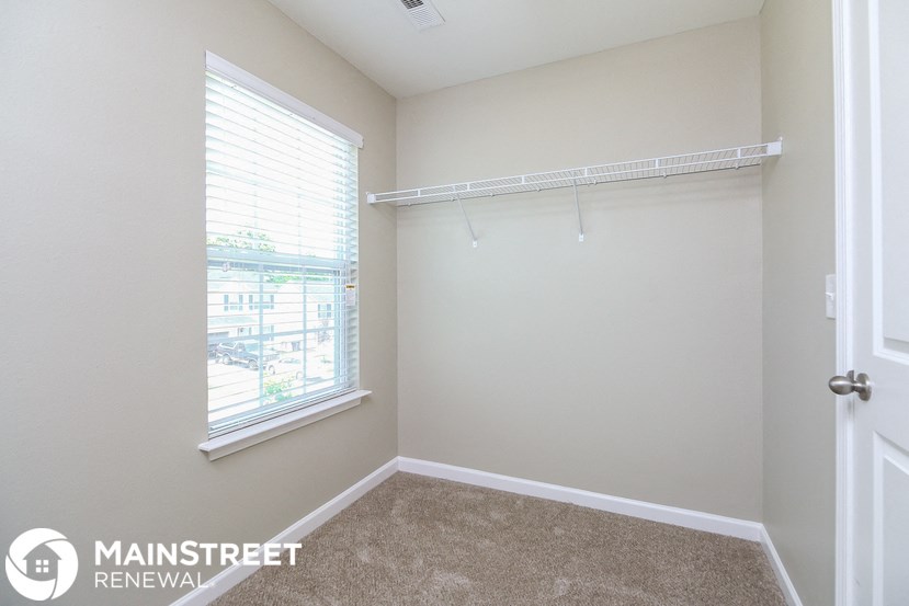 a room with a closet and a window and a white wall with a hanging rail