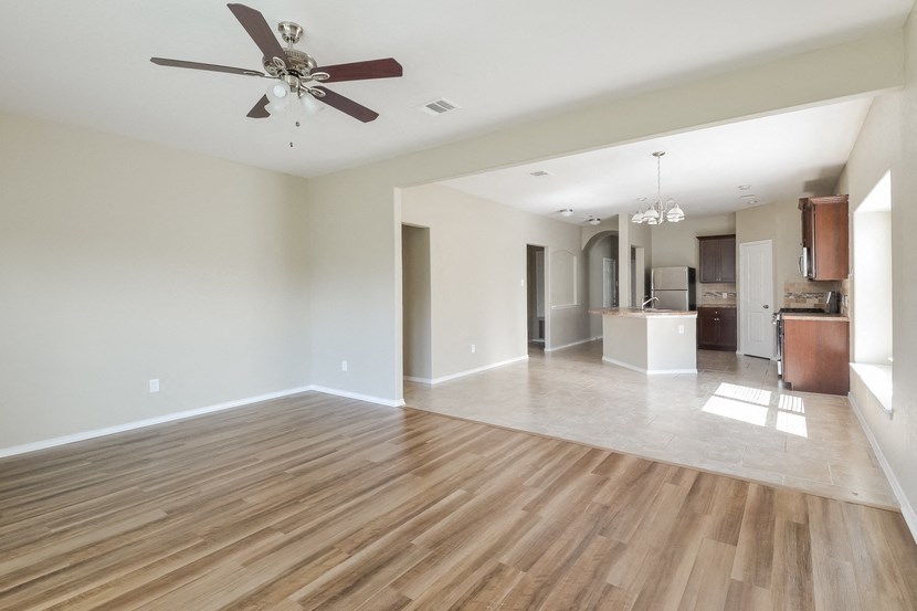 an empty living room with a ceiling fan and a kitchen