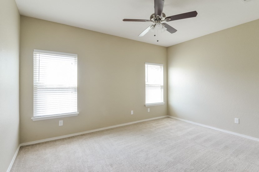 an empty room with a ceiling fan and two windows