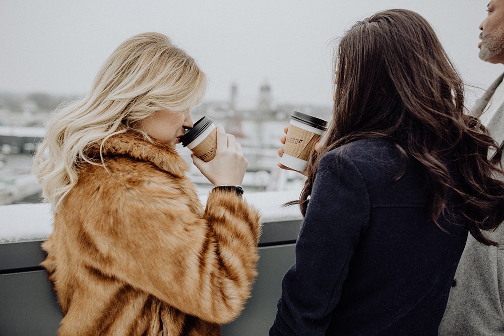 two women drinking coffee on a balcony with a view of the city