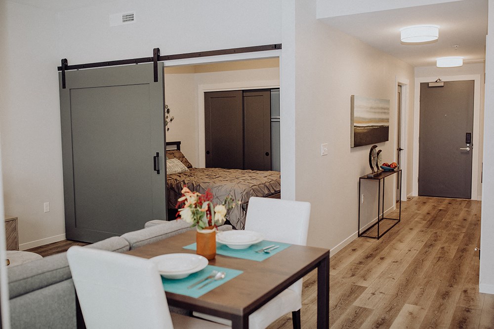 a bedroom with a sliding door to a living room with a table and chairs
