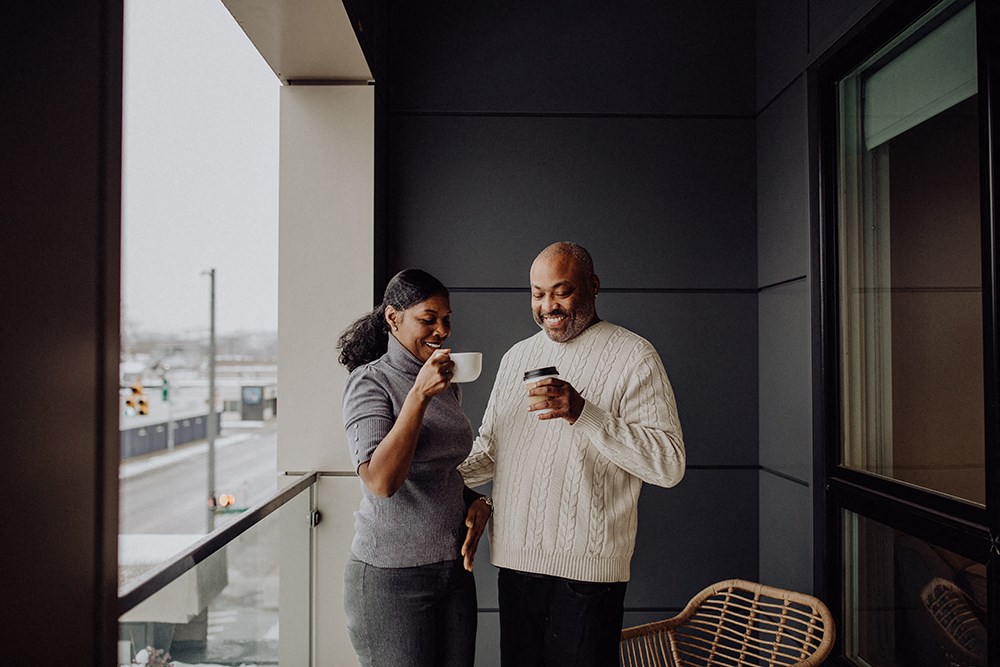 a man and a woman standing on a balcony holding a cup of coffee