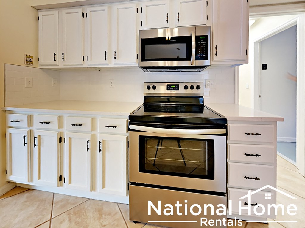 A white kitchen with a black stove and microwave.