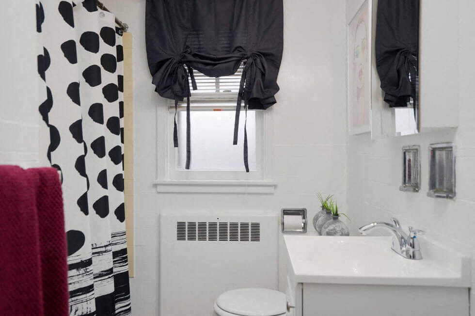 a white bathroom with a black and white shower curtain and a window