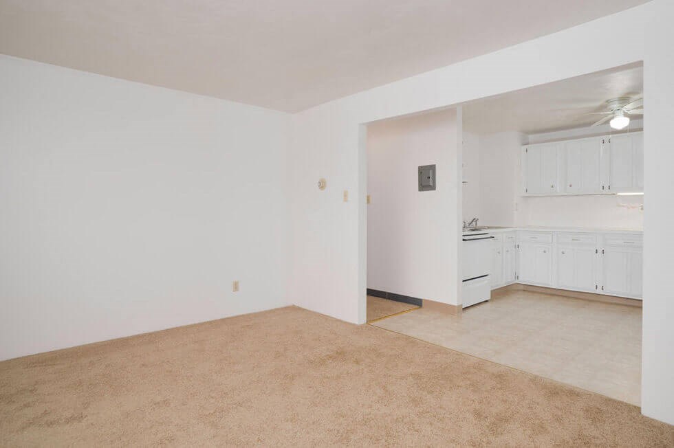an empty living room and kitchen with white walls and carpet