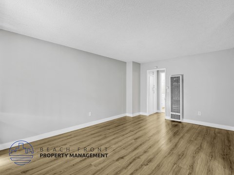 A spacious room with wooden flooring and white walls, with a door on the right side.