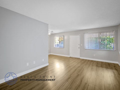 A room with wooden flooring and white walls, with a window covered by vertical blinds.
