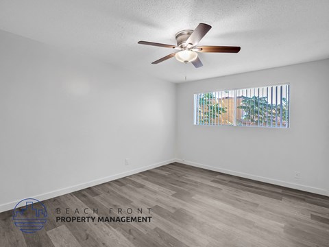 A room with a ceiling fan and a window showing a view of a building and trees.