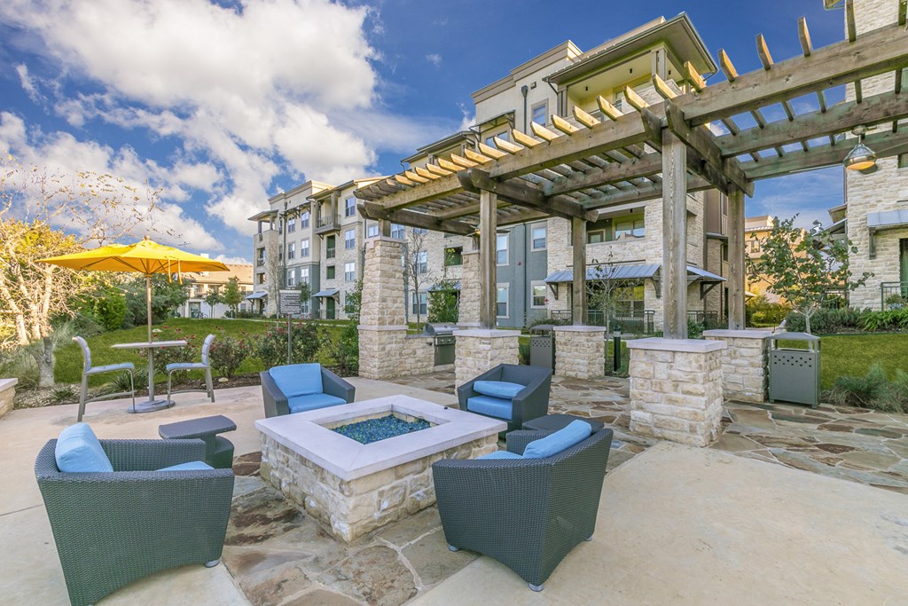 a patio with chairs and a fire pit and a building in the background