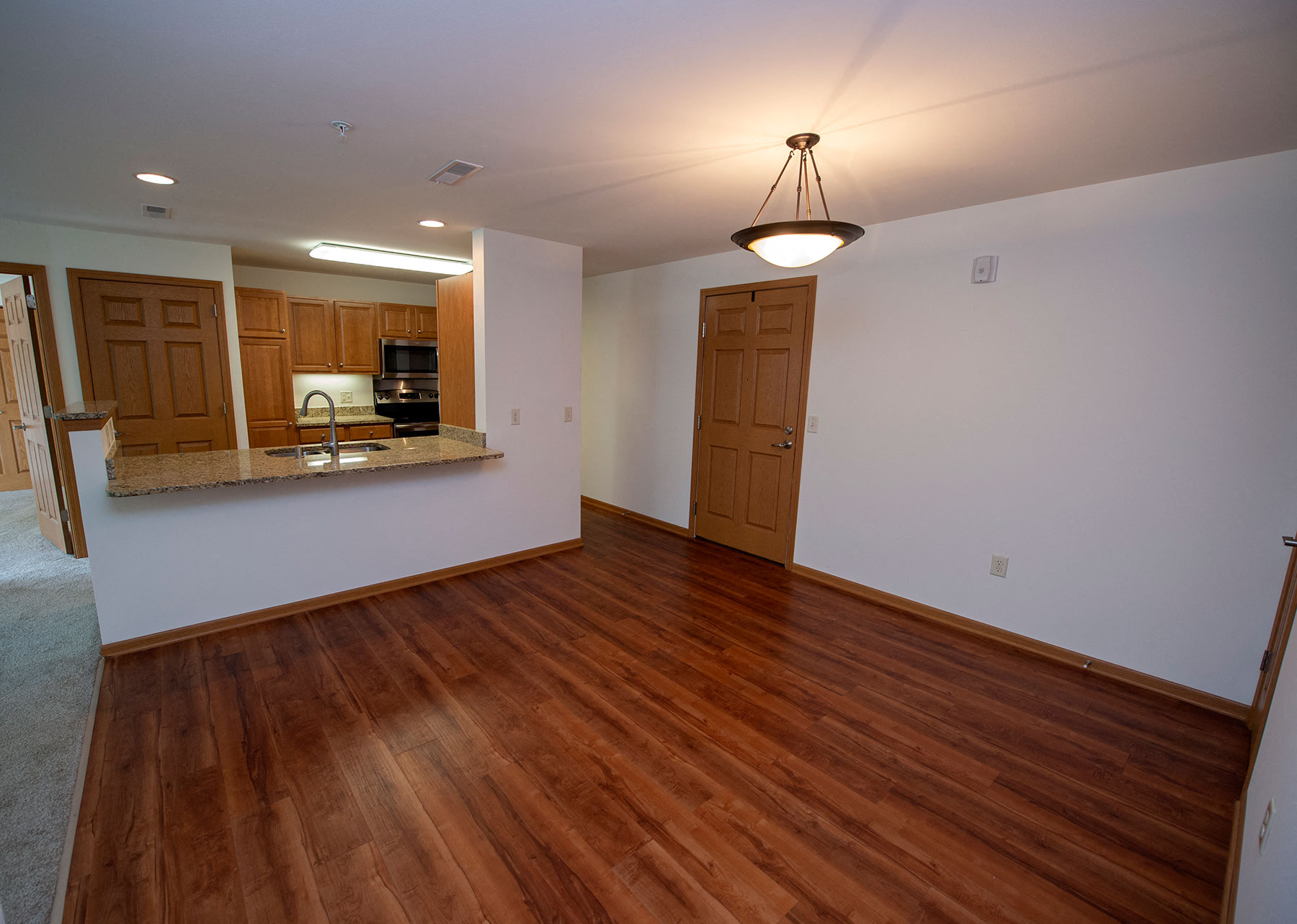 an empty living room with wood flooring and a kitchen