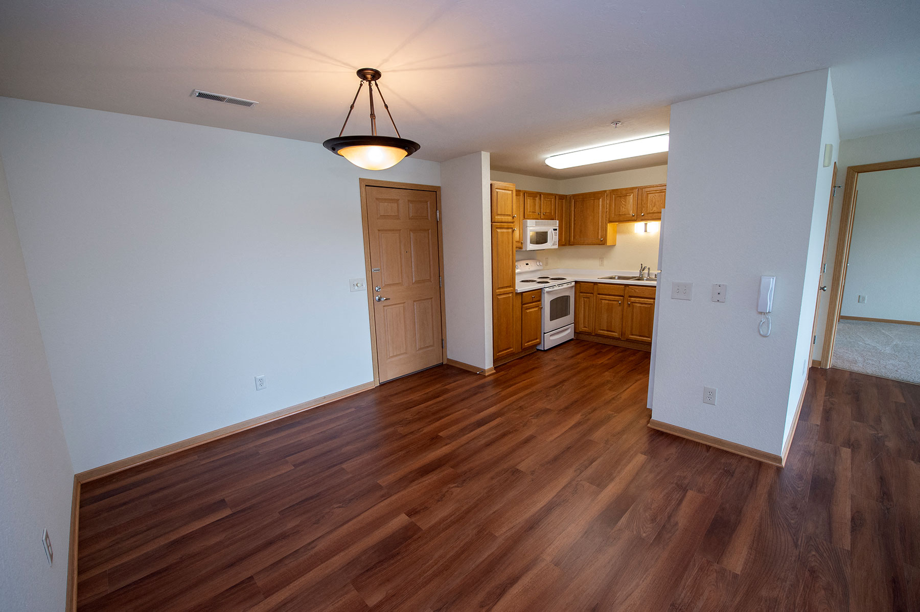 an empty living room with wood flooring and a kitchen